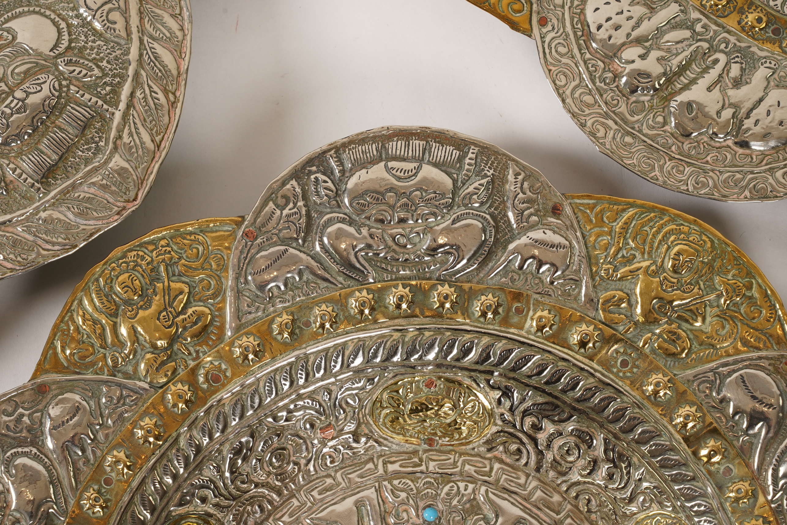 A graduated set of three Nepalese repoussé white metal and brass chargers, first half 20th century